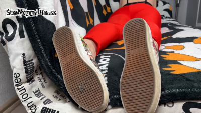 Brunette Crossed Legs In Yoga Pants Lying On Sofa In Stinky Shoes- Sniff The Smell Of Stinky Boots, Sweaty Insoles In Sneakers, Girl Ignores Smoking, Pointing Long Toes With Black Pedicure